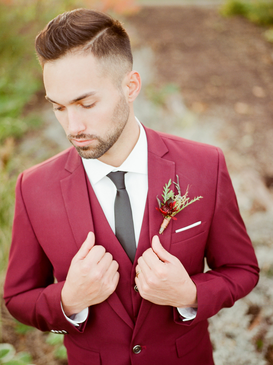 A groom wears a red suit and is photographed