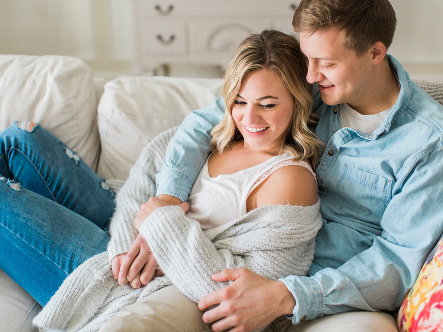 A couple cuddles on the couch during their intimate in-home engagement session by Love Tree Studios.