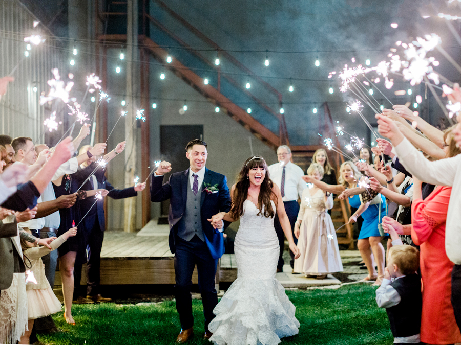 Guests cheer and hold sparklers as the bride and groom exit the reception photographed by missouri wedding photographer Love Tree Studios at a Camdenton Missouri wedding.