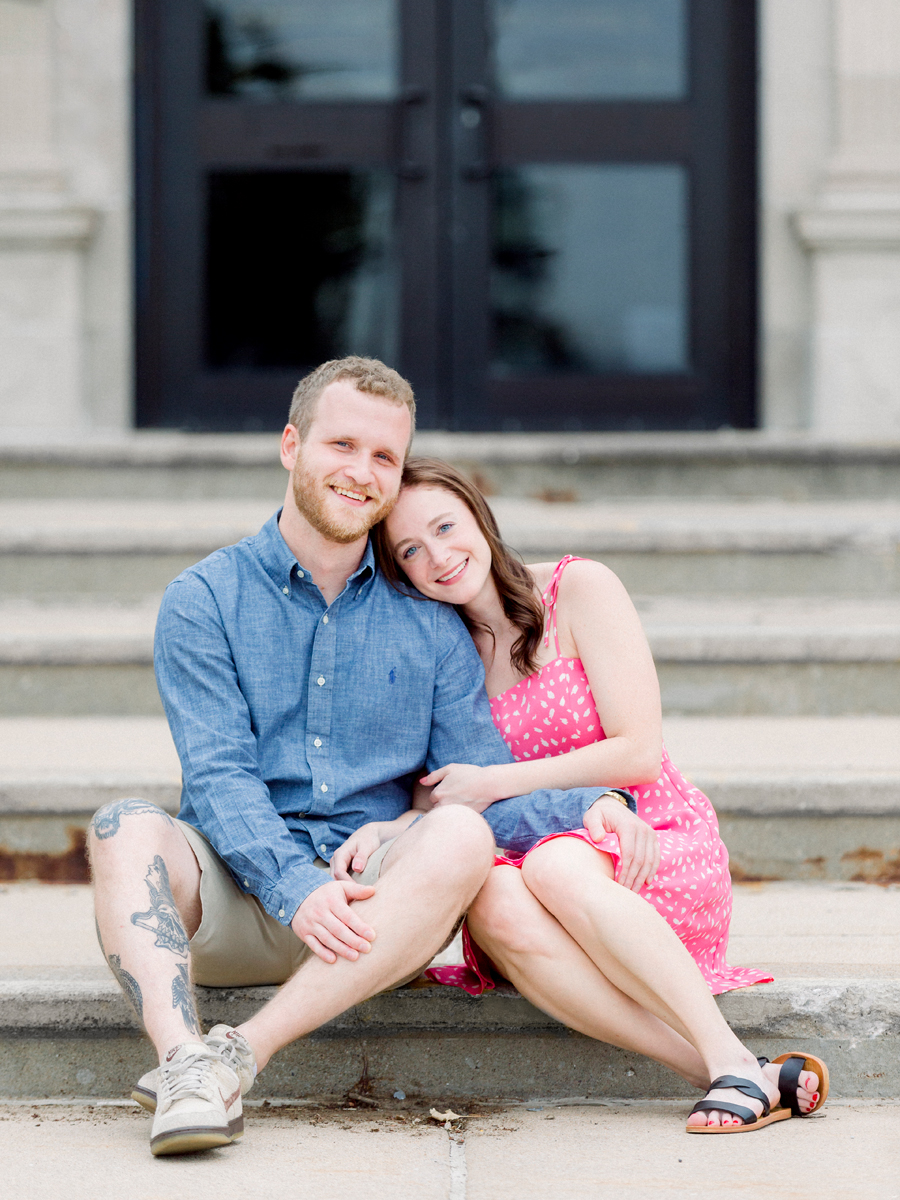 A couple poses on the steps of Hickman Highschool during their engagement session.