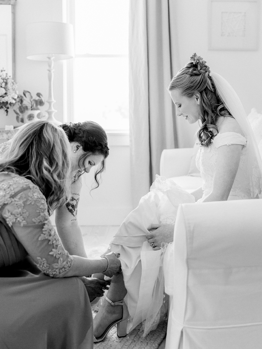A bride puts her shoes on in the bridal cottage at a Blue Bell Farm wedding by Love Tree Studios.