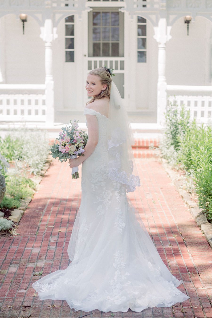 A bride looks back at the camera in front of the farm house at a Blue Bell Farm wedding by Love Tree Studios.