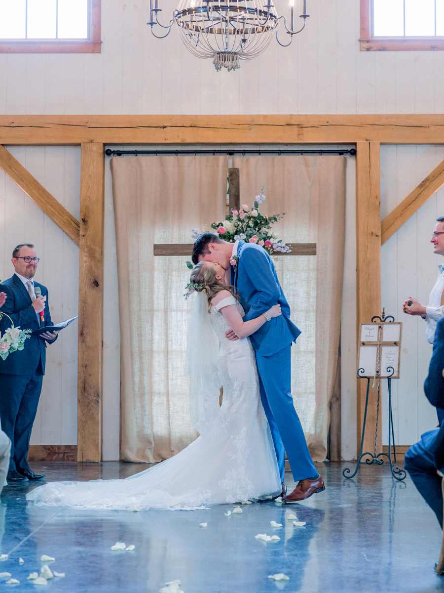 A bride and groom kiss during their ceremony in the barn at a Blue Bell Farm wedding by Love Tree Studios.