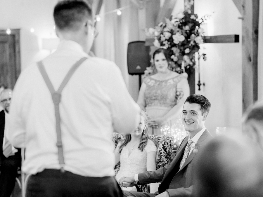 The groom smiles at the best man as he gives at toast at a Blue Bell Farm wedding by Love Tree Studios.