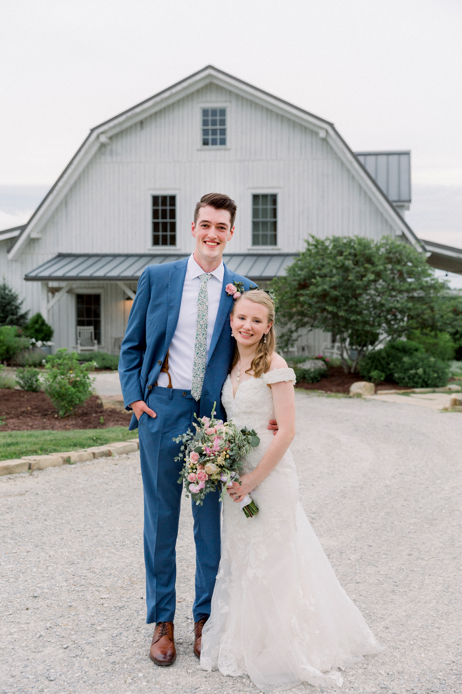 A bride and groom smile at the camera in front of the barn at a Blue Bell Farm wedding by Love Tree Studios.