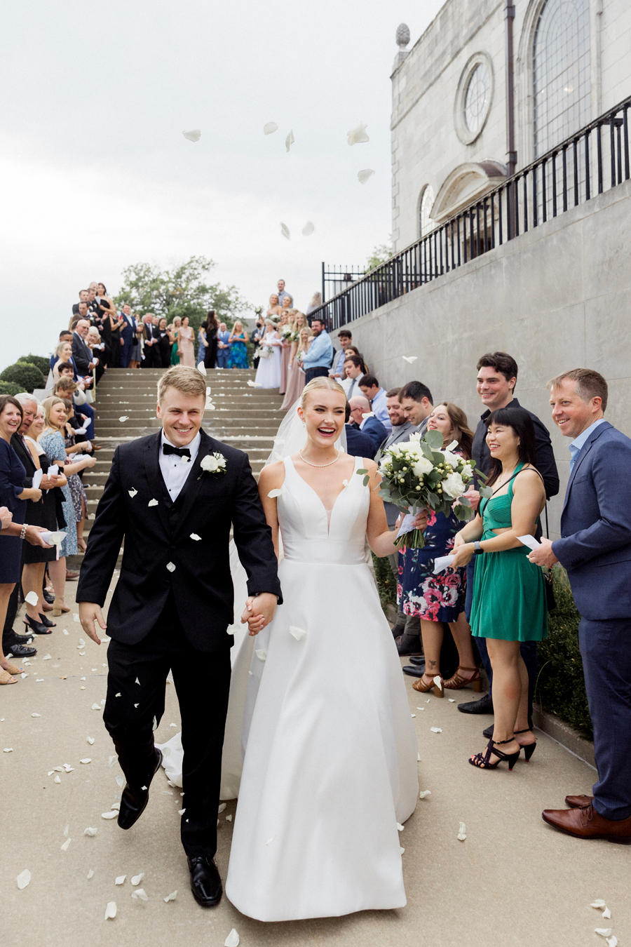 Guest throw petals as the bride and groom exit the Church of St. Mary, Aldermanbury at a Westminster College wedding by Love Tree Studios.