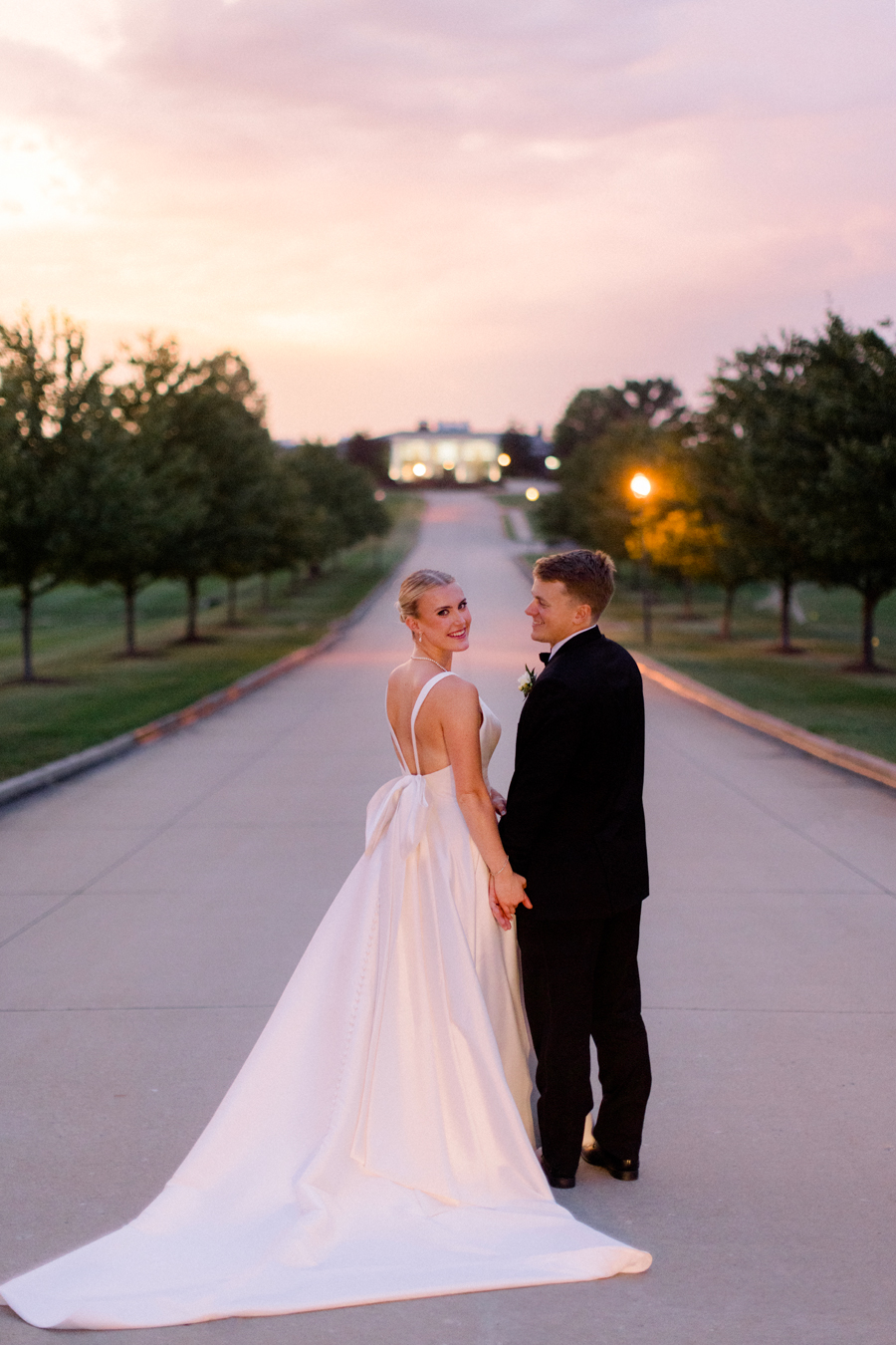 A bride and groom walk hand in hand as the sun sets over the Club at Old Hawthorne for their Westminster College wedding by Love Tree Studios.