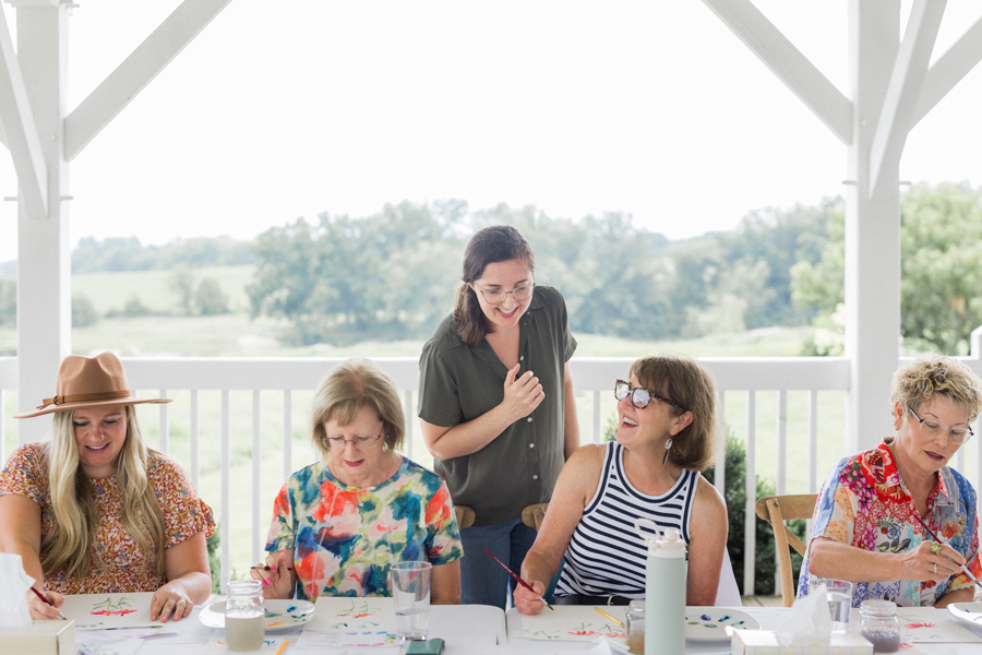 Friends laughing and encouraging each other’s artwork, capturing the camaraderie at the paint and picnic event.