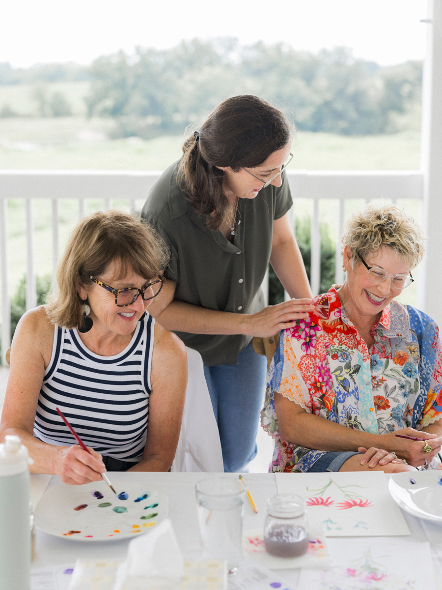 Friends laughing and encouraging each other’s artwork, capturing the camaraderie at the paint and picnic event.