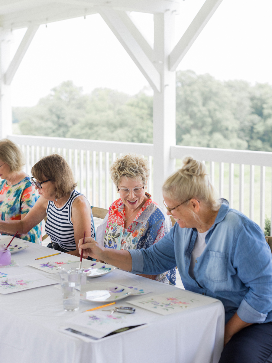 Friends laughing and encouraging each other’s artwork, capturing the camaraderie at the paint and picnic event.