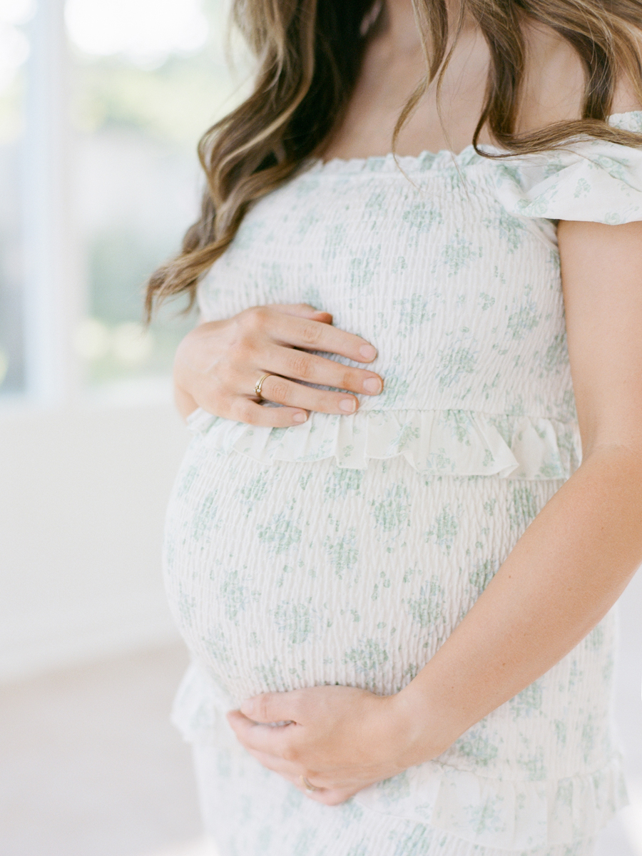 Close-up of expectant mother’s hands gently resting on her belly during a family maternity session in the Garden Studio by Love Tree Studios in Columbia, Missouri.