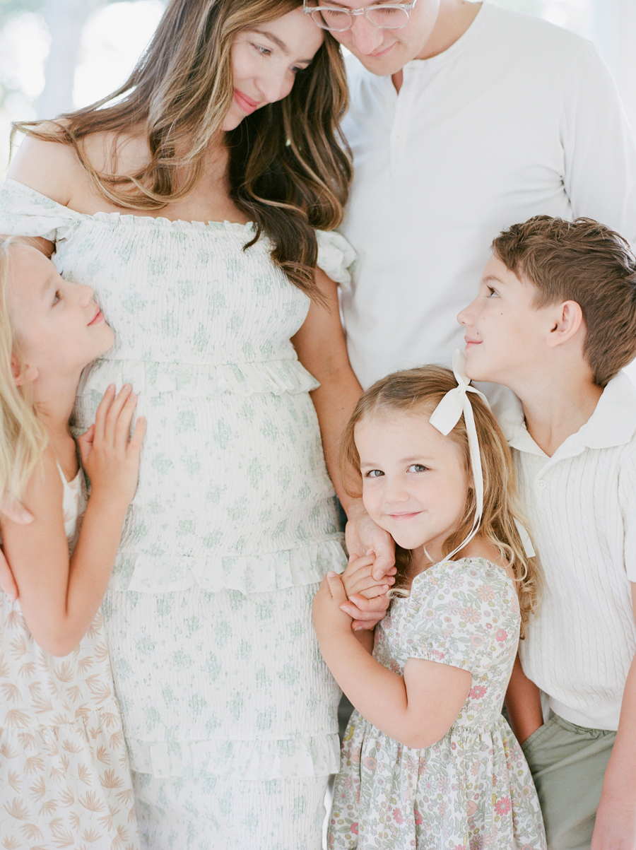 The youngest daughter smiles at the camera while celebrating the upcoming addition of a new baby during a family maternity session by Love Tree Studios.