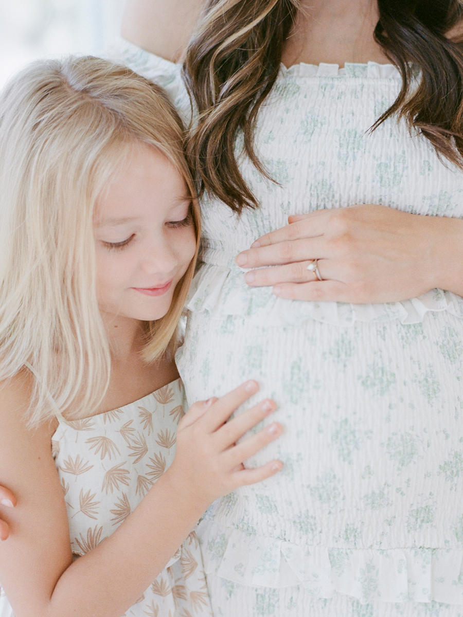 Close-up of a daughter's hands gently resting on mom's belly during a family maternity studio session in Columbia, Missouri by photographer Love Tree Studios.