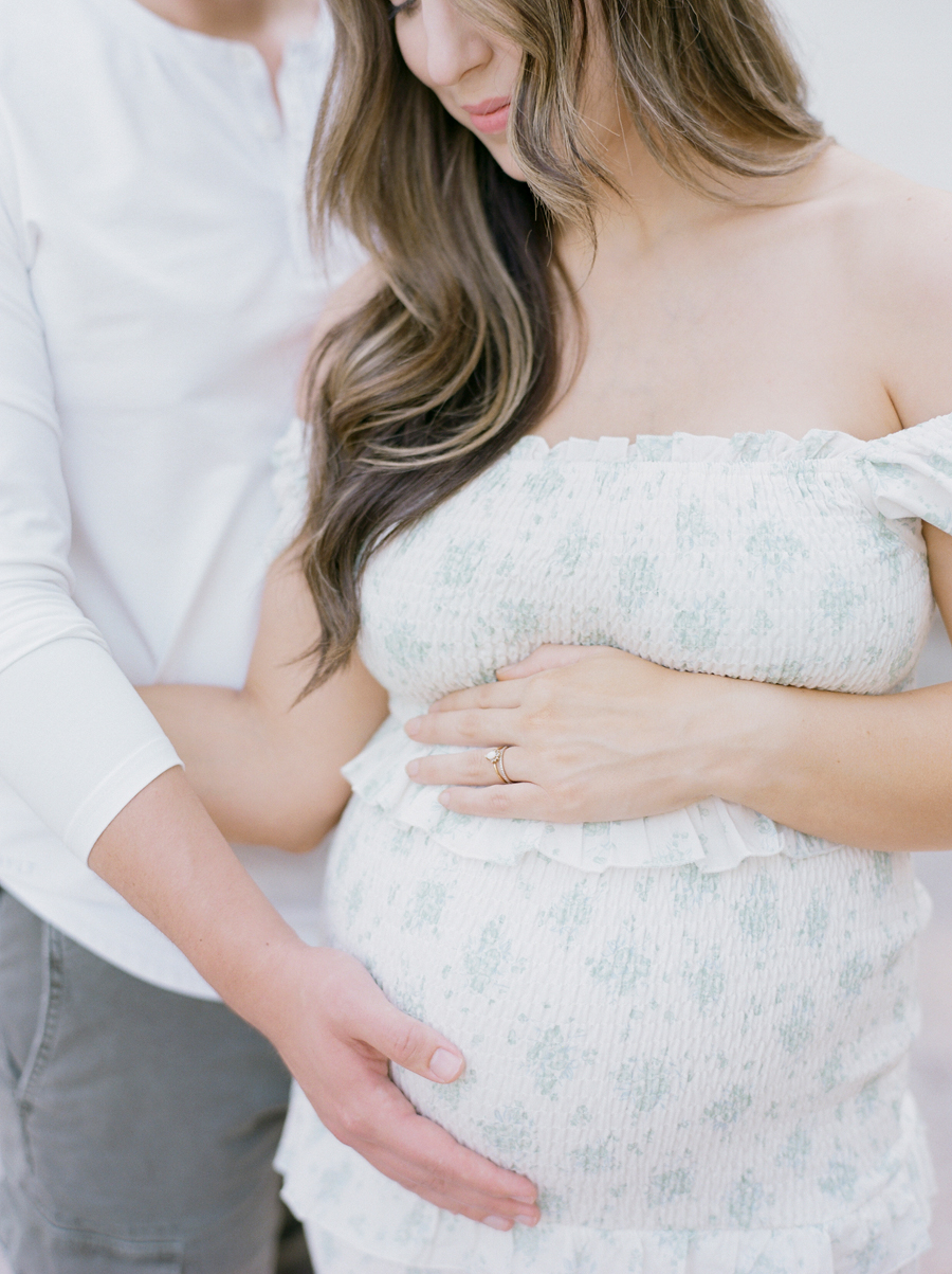 Close-up of the Bedford family's hands gently placed on the baby bump during their outdoor Garden Studio family maternity session in Columbia, Missouri by Love Tree Studios.