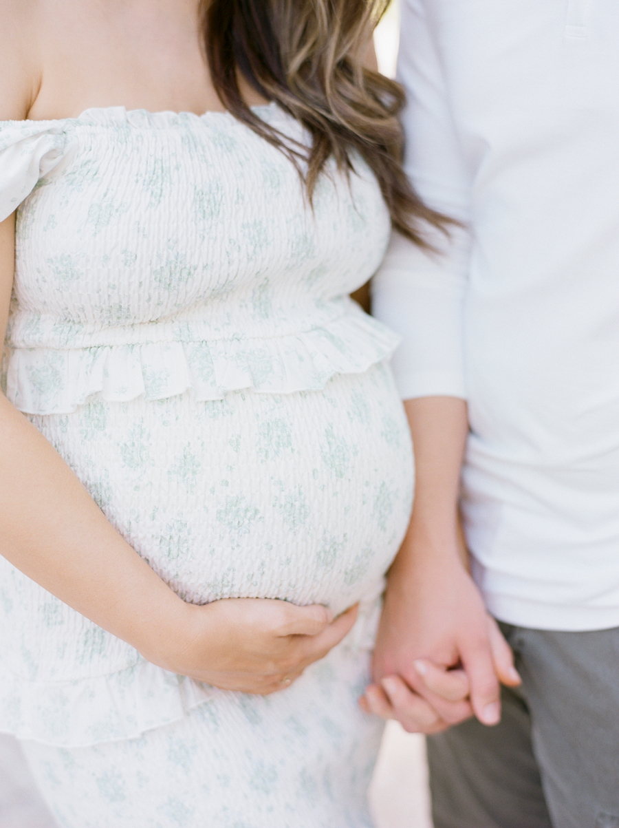 Close-up of expectant mother’s hands gently resting on her belly while holding her husband's hand during a family maternity session at Love Tree Studio's Garden Studio in Columbia, Missouri.