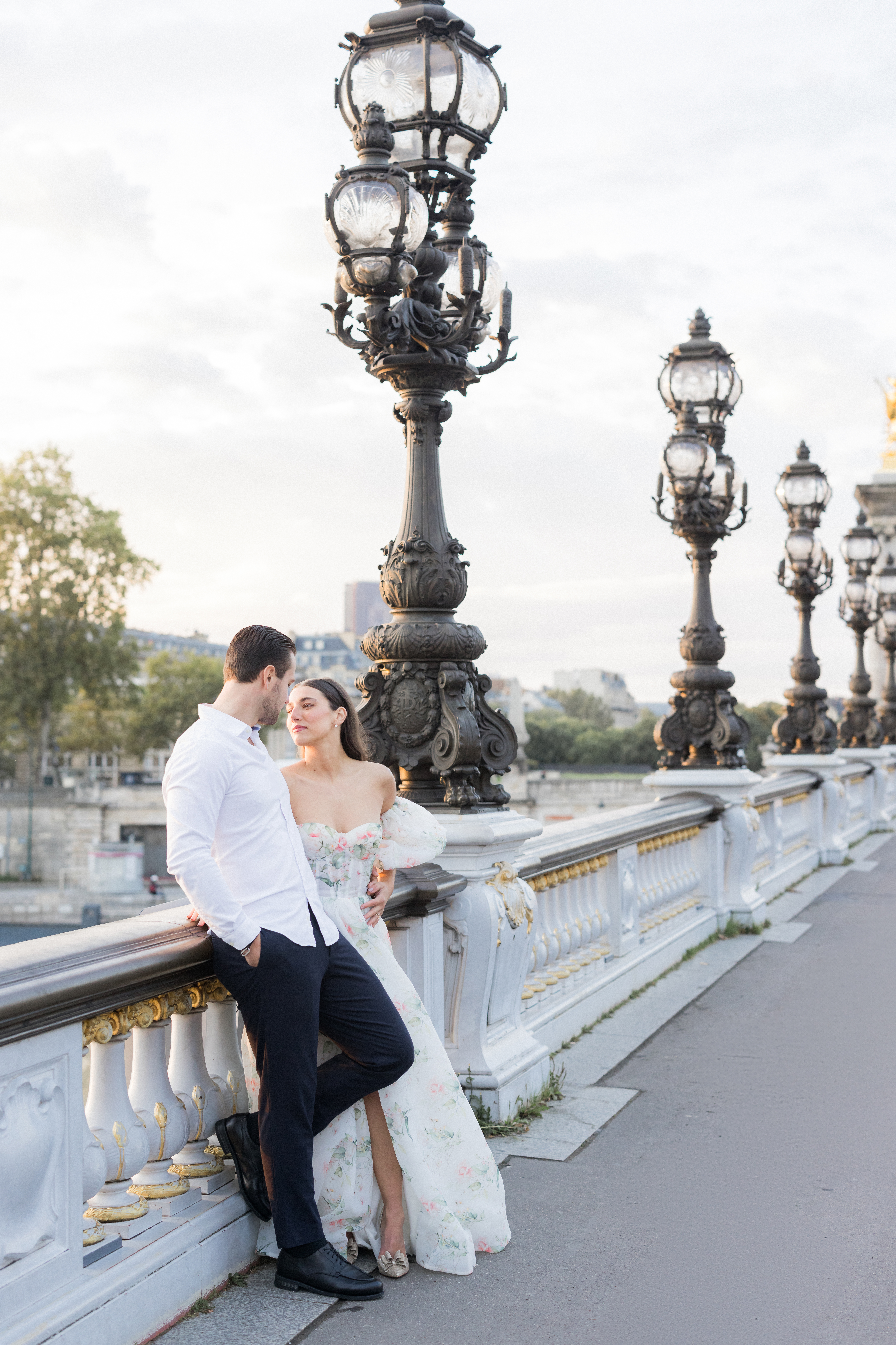 Wide-angle shot of Sinaï and Abraham on the ornate Pont Alexandre III Bridge, surrounded by golden light during their Paris portrait session.