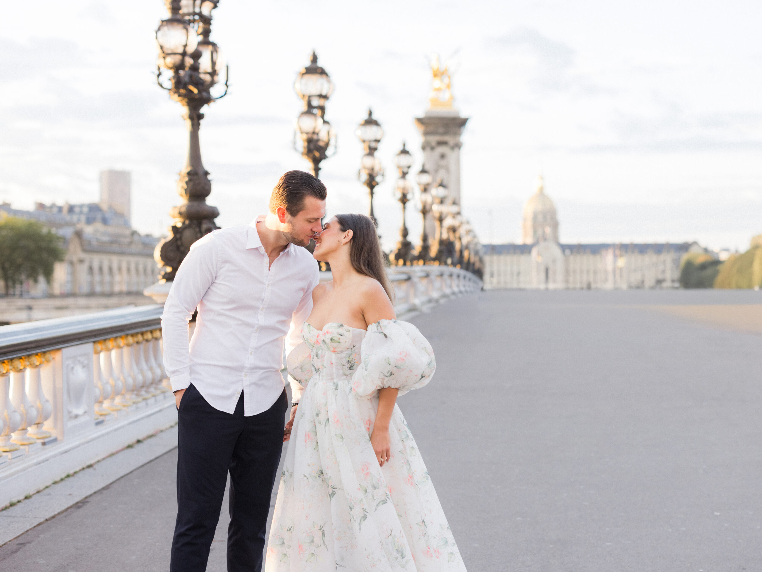 Abraham leaning in to kiss Sinaï’s forehead as they stand near the ornate bridge railing.