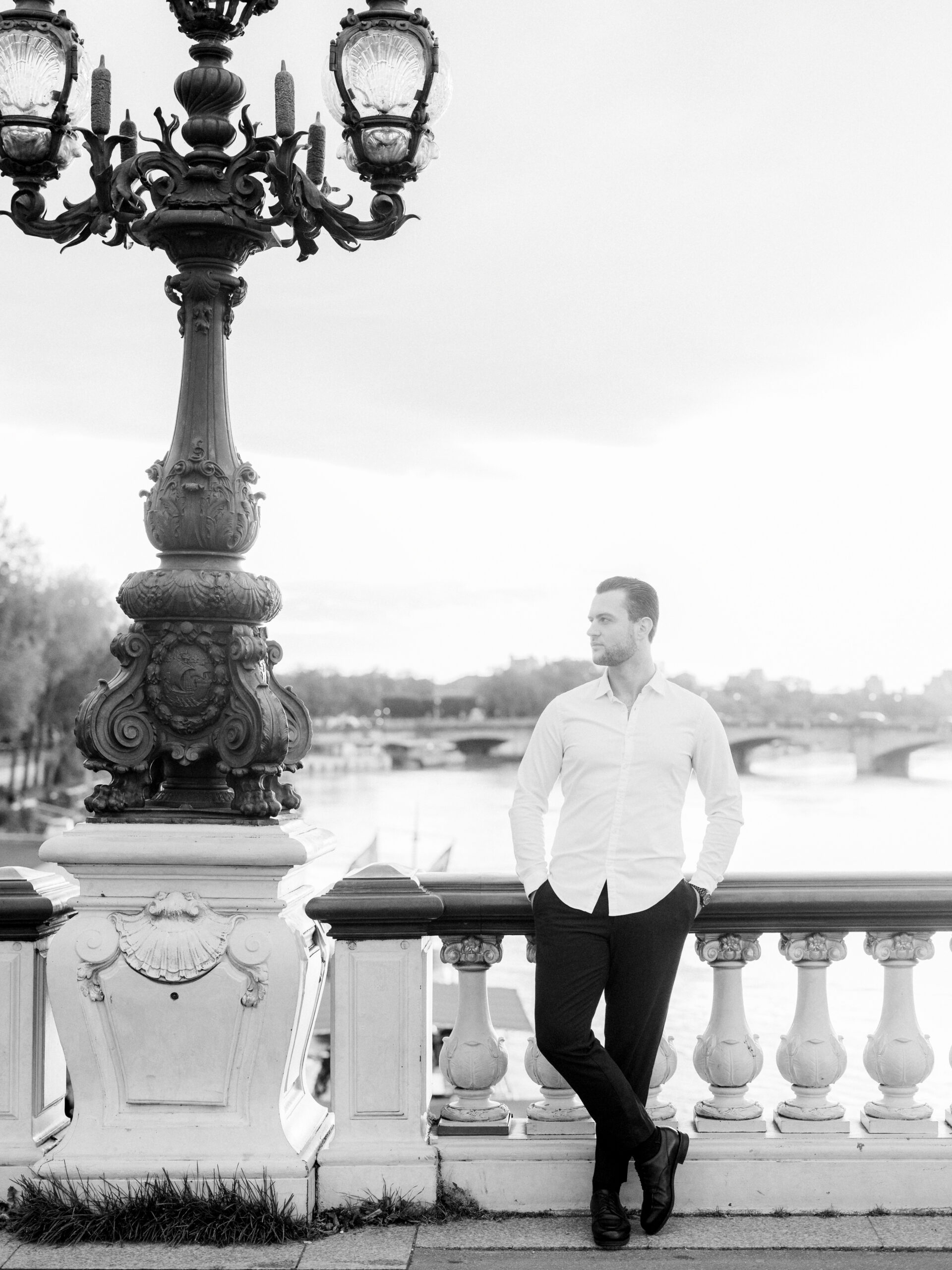 Abraham leaning against the ornate railing of Pont Alexandre III Bridge, with the Seine flowing below.