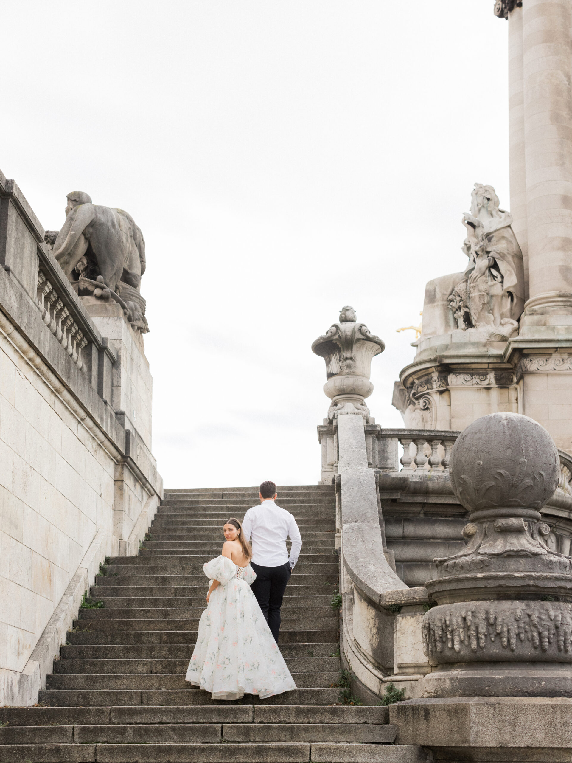 Sinaï’s floral gown trailing behind as she and Abraham ascend the steps of Pont Alexandre III Bridge during their Paris portrait session Love Tree Studios.