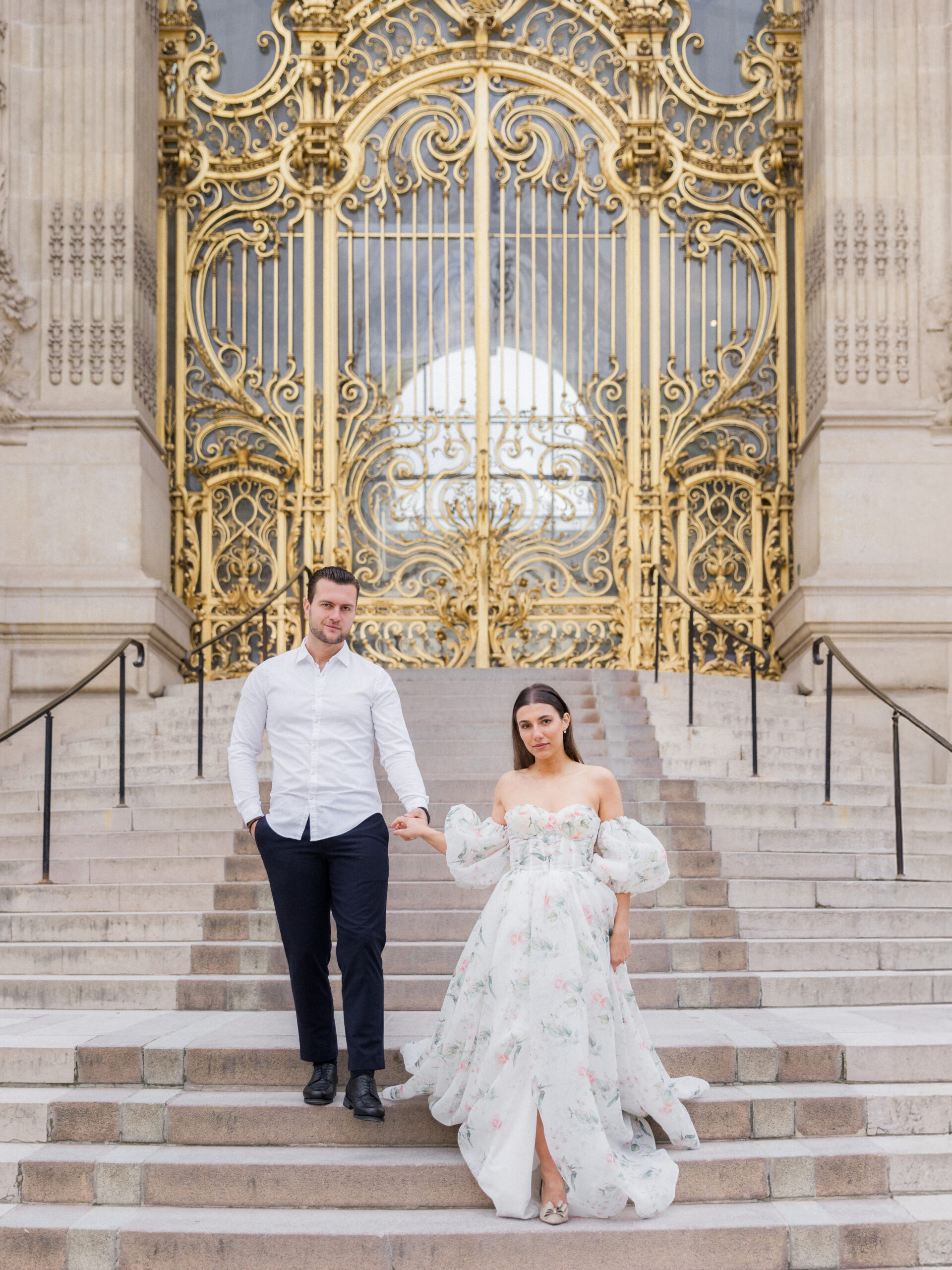 Sinaï and Abraham holding hands, framed by the intricate details of the golden gate during their Paris portrait session.