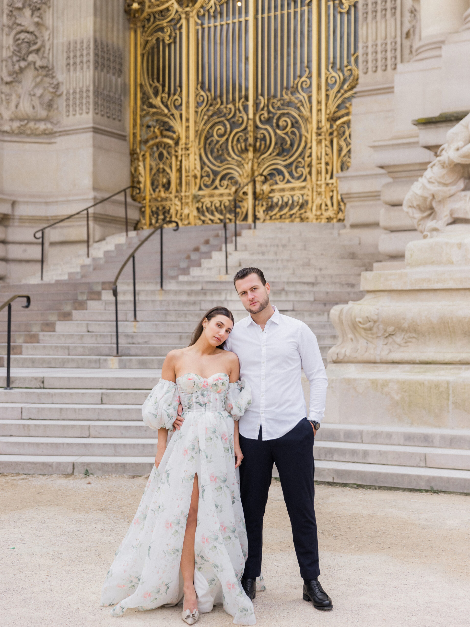 Sinaï in a floral gown, standing in front of the grand golden gate at La Petite Palace.