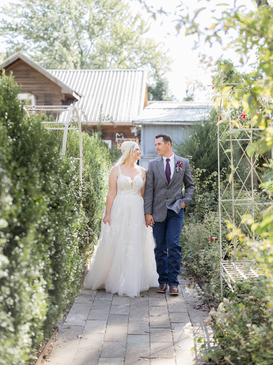 Bride and groom strolling through the gardens at Alpine Park during their chic Western Missouri wedding, captured by Love Tree Studios.