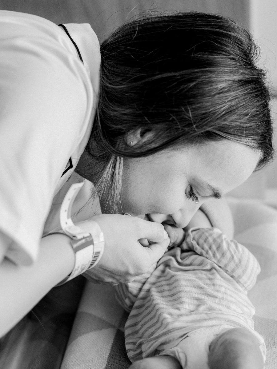 Close-up of a mom kissing her newborn’s fingers during a Fresh 48 session, showing delicate details in soft black and white, captured by Love Tree Studios.