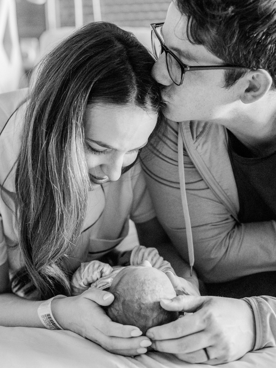 Parents holding their newborn gently during a Fresh 48 session, a timeless moment captured in black and white.