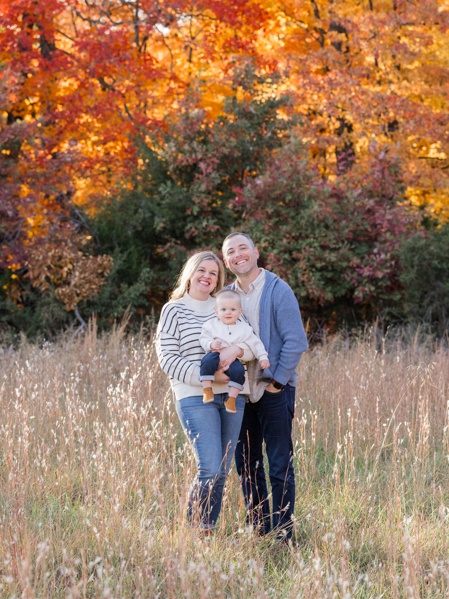 Parents holding baby under colorful fall trees, showcasing vibrant family photography by Love Tree Studios in Columbia, MO.