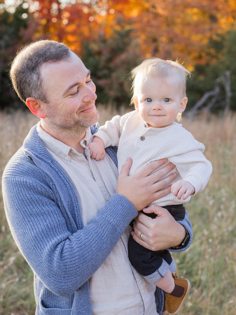 Father and baby smiling under fall trees during an outdoor session by Love Tree Studios in Columbia, MO.