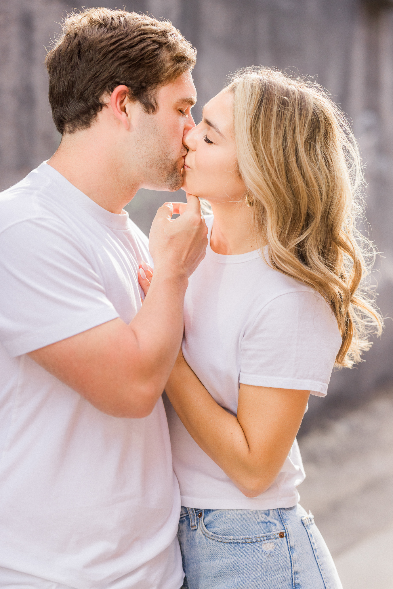 Couple kissing in soft sunlight wearing white t-shirts and jeans during their spring engagement photos in Missouri.