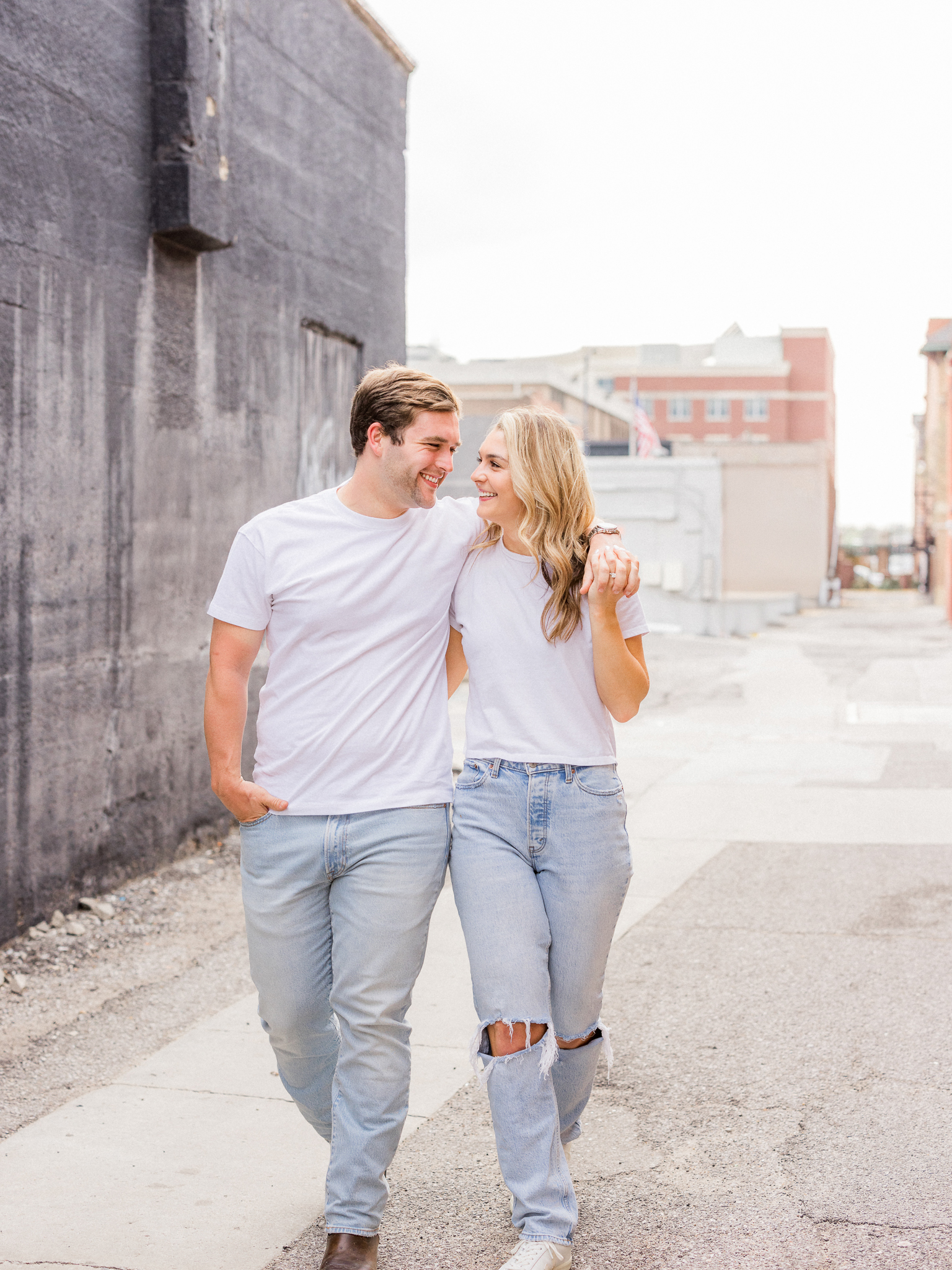 Playful engagement moment as the couple smiles at each other while holding hands in downtown Missouri.