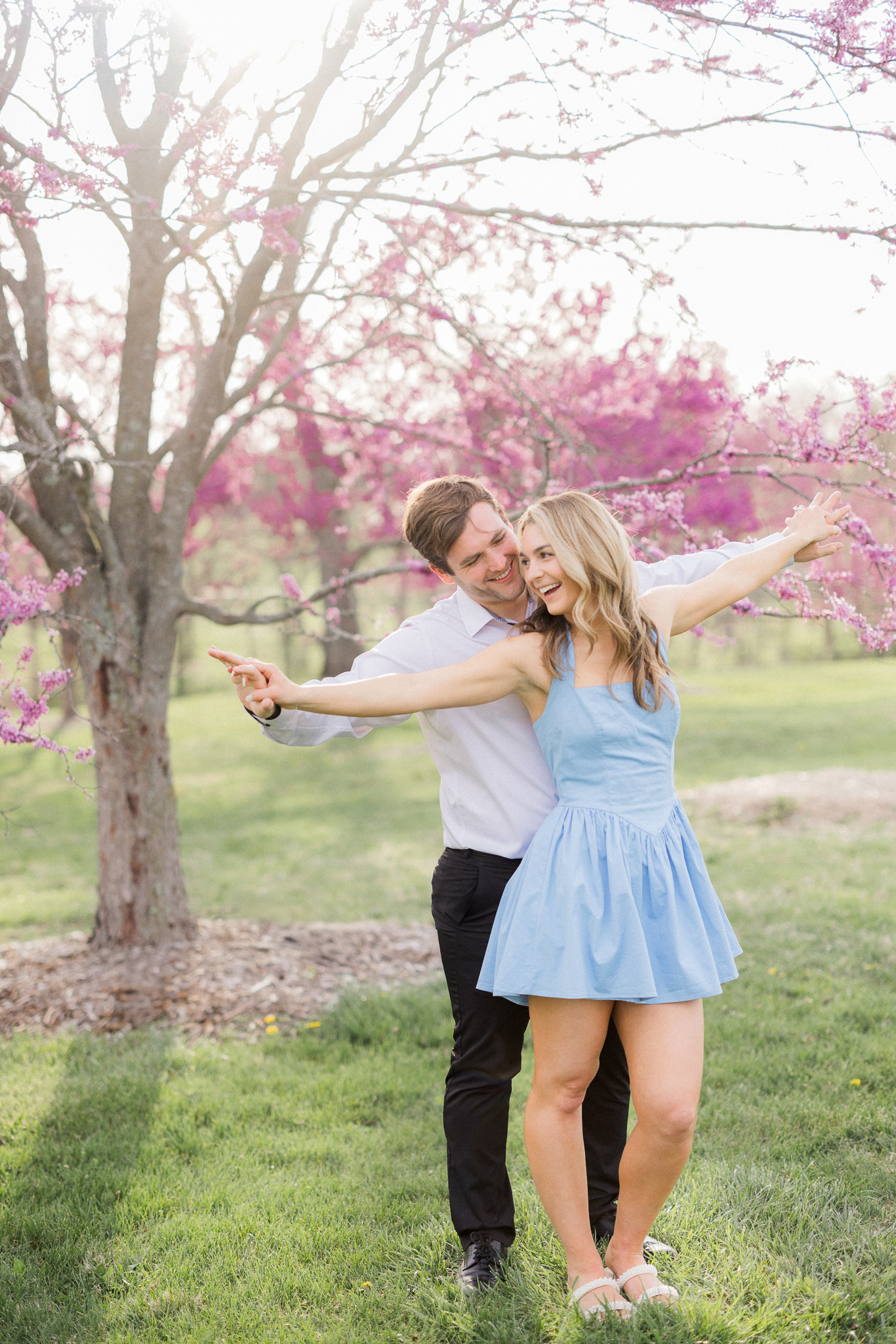 Couple spinning together beneath blooming redbud trees in the park for their spring engagement photos in Missouri.