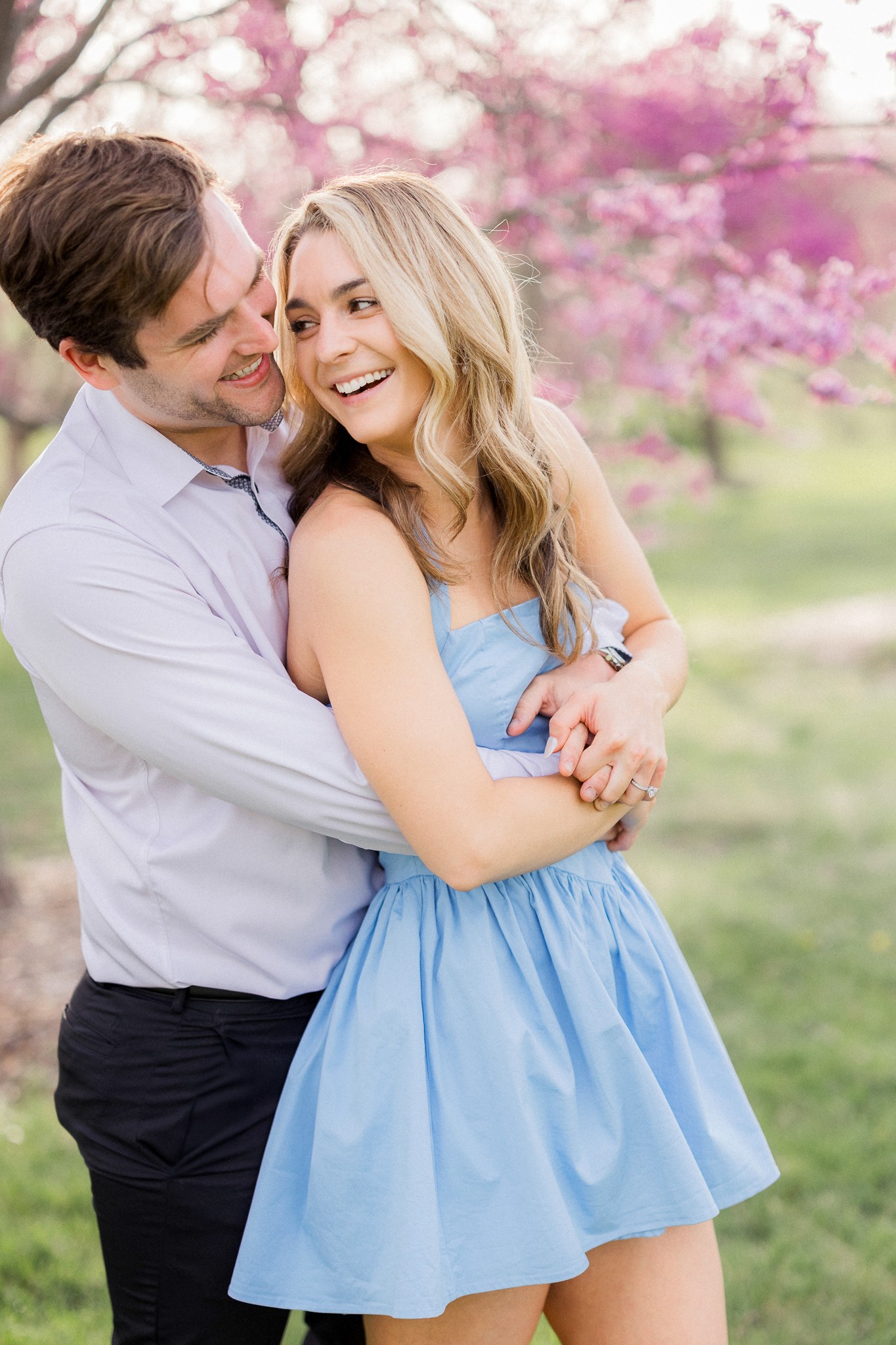 Groom-to-be looking lovingly at his fiancée in front of colorful blooming trees during their park session.