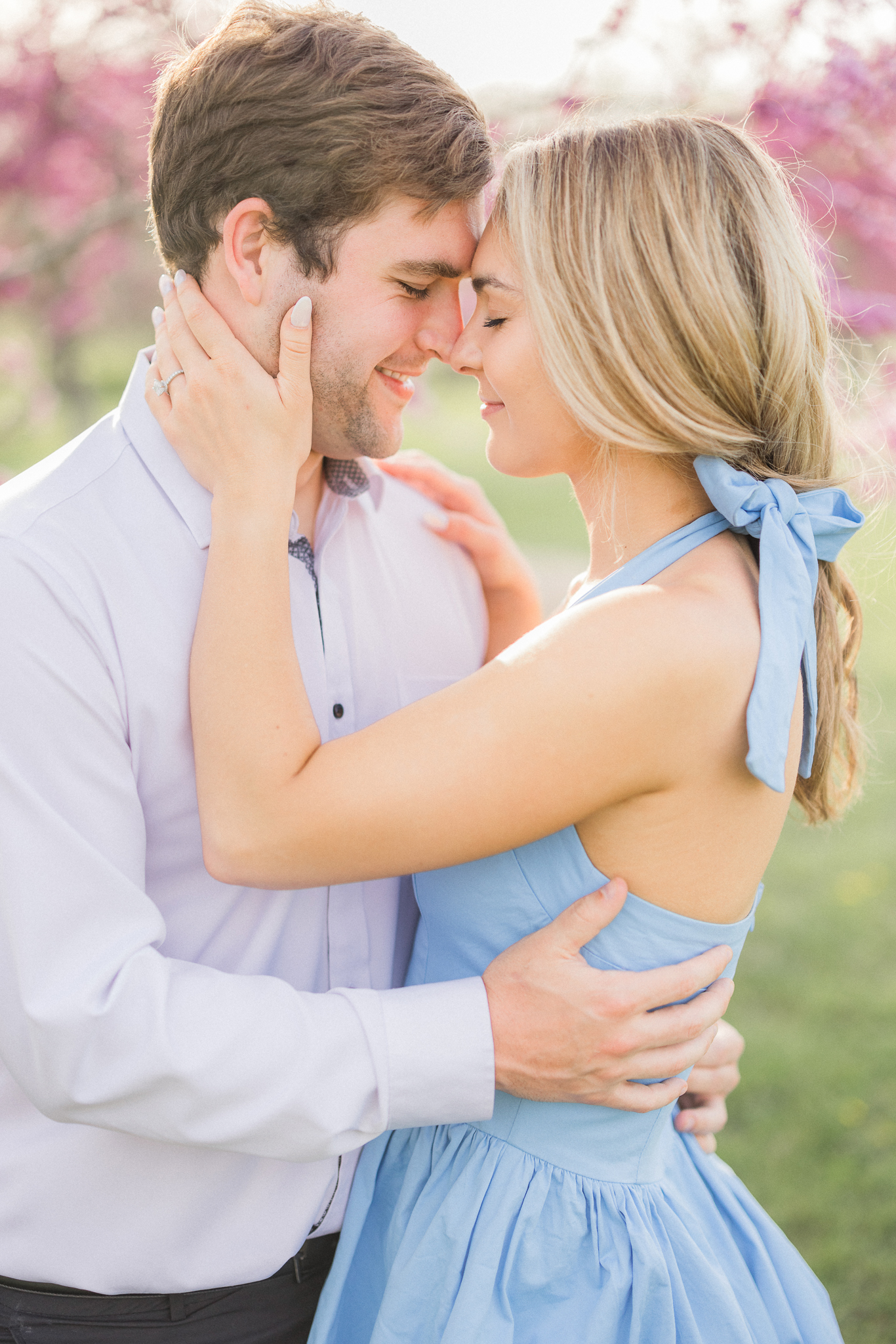 Romantic forehead-to-forehead photo of the engaged couple framed by soft spring light and blooms.

