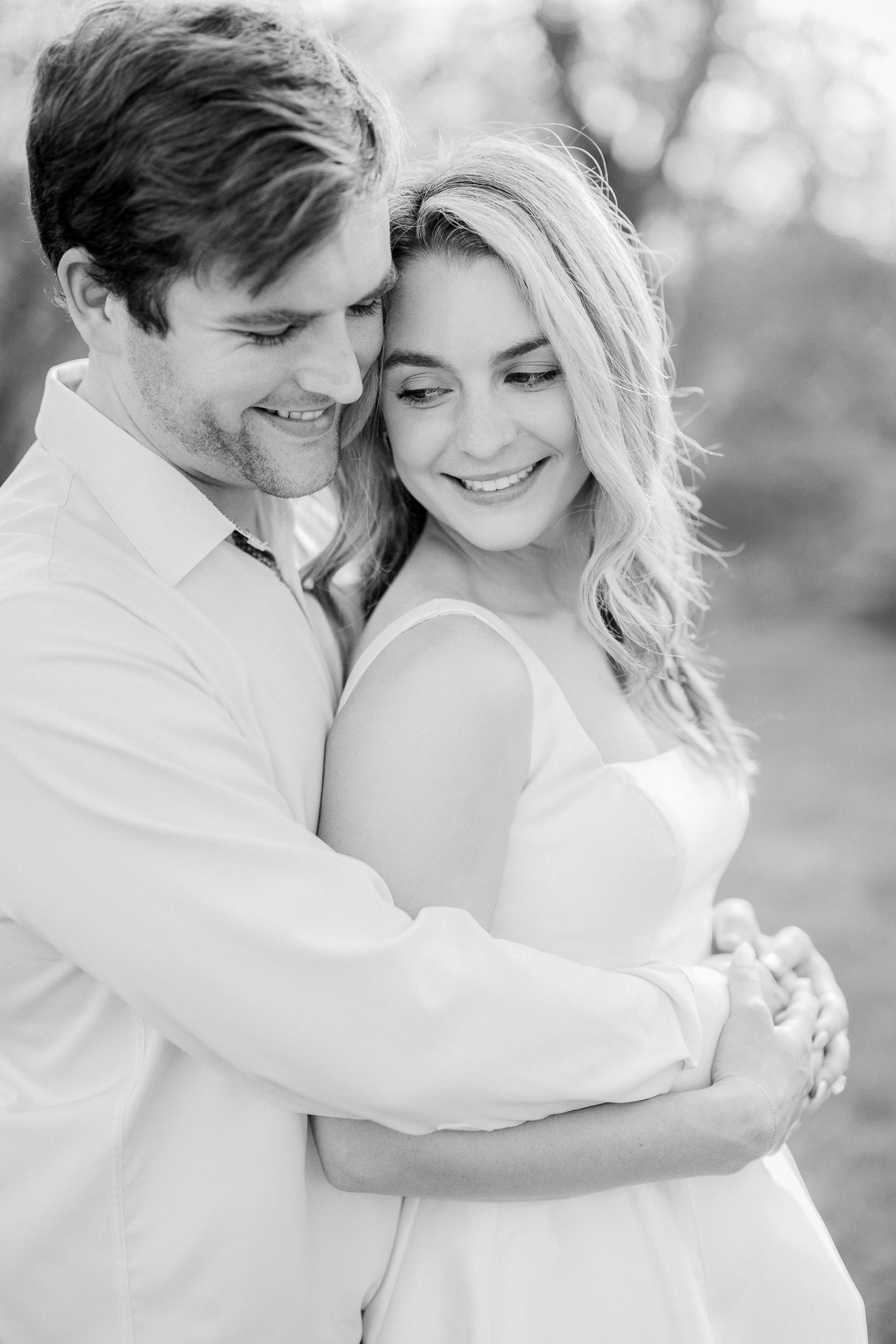 Bride-to-be gazing confidently as her fiancé gently holds her during golden hour.