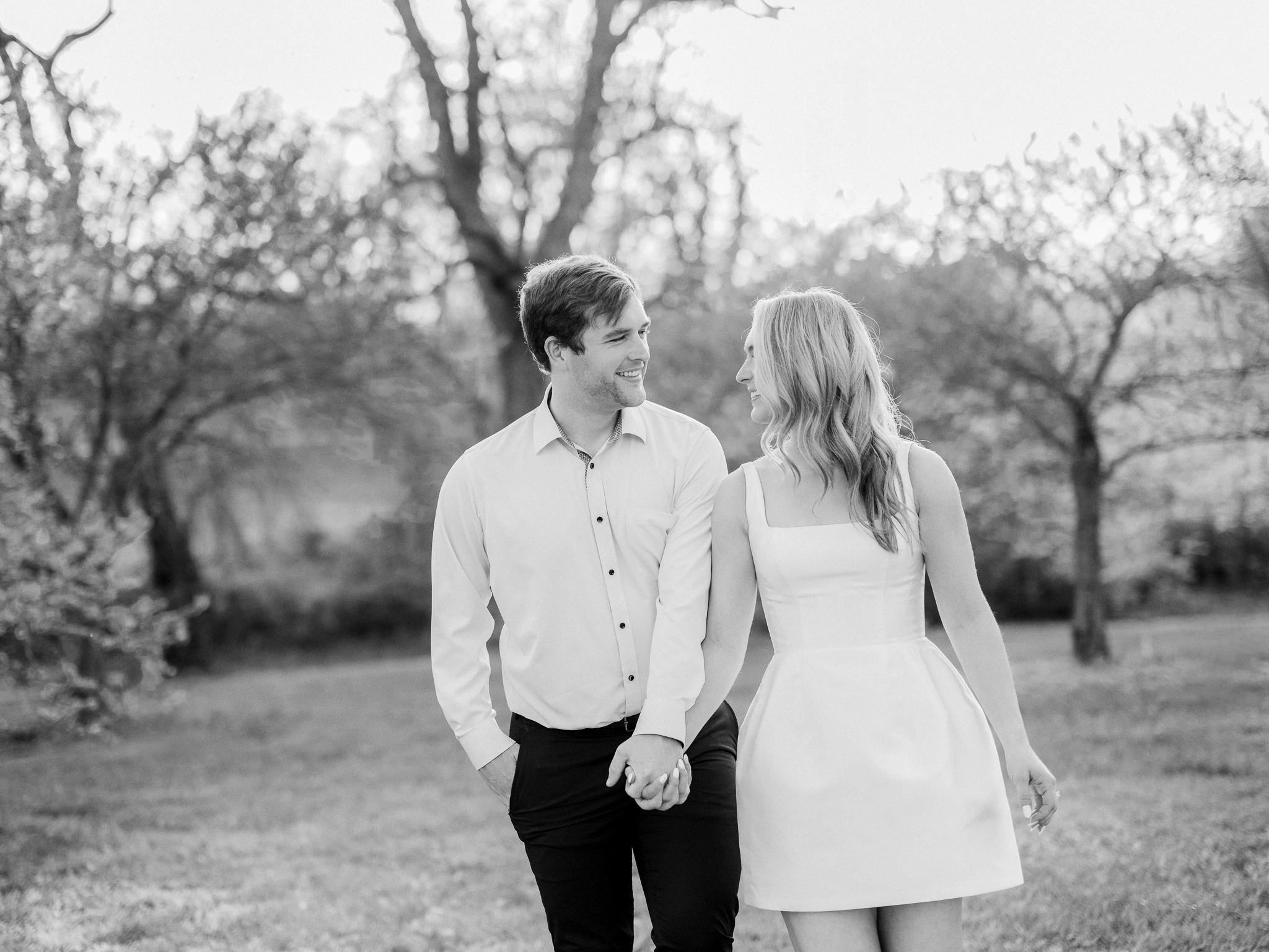 Wide shot of the couple standing close together, surrounded by vivid spring redbud trees in full bloom.