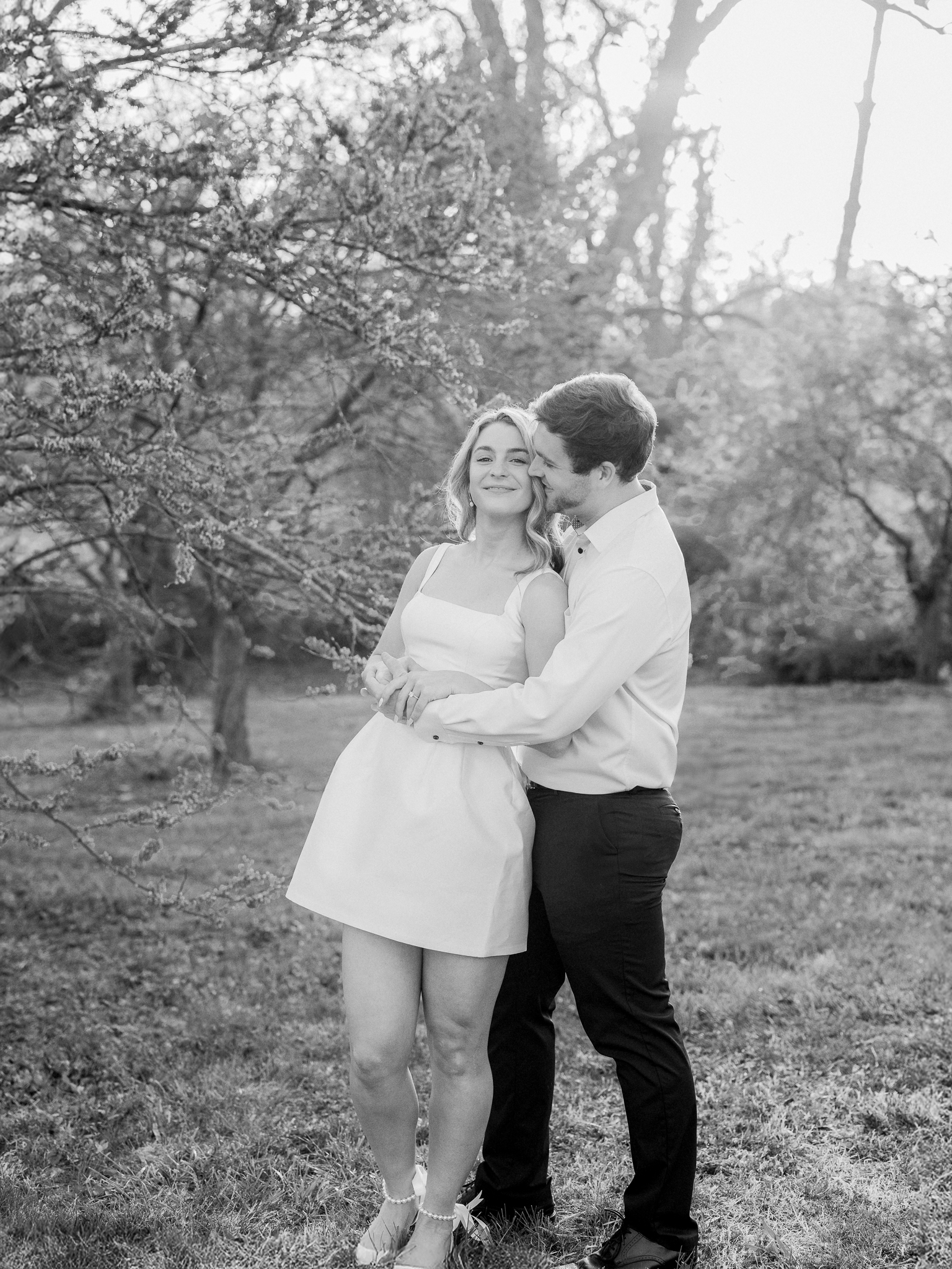 Bride-to-be laughing as her fiancé wraps her in a hug surrounded by spring flowers.