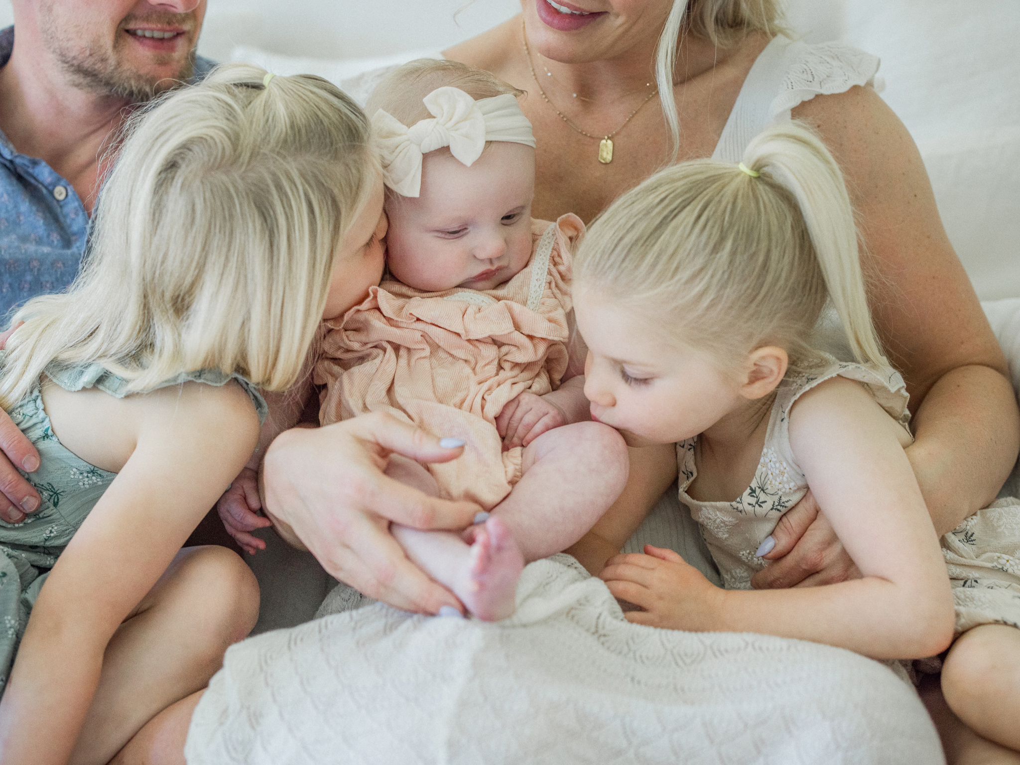 Big sisters showering baby Lenny with kisses during a Missouri in-home newborn lifestyle session by Love Tree Studios.