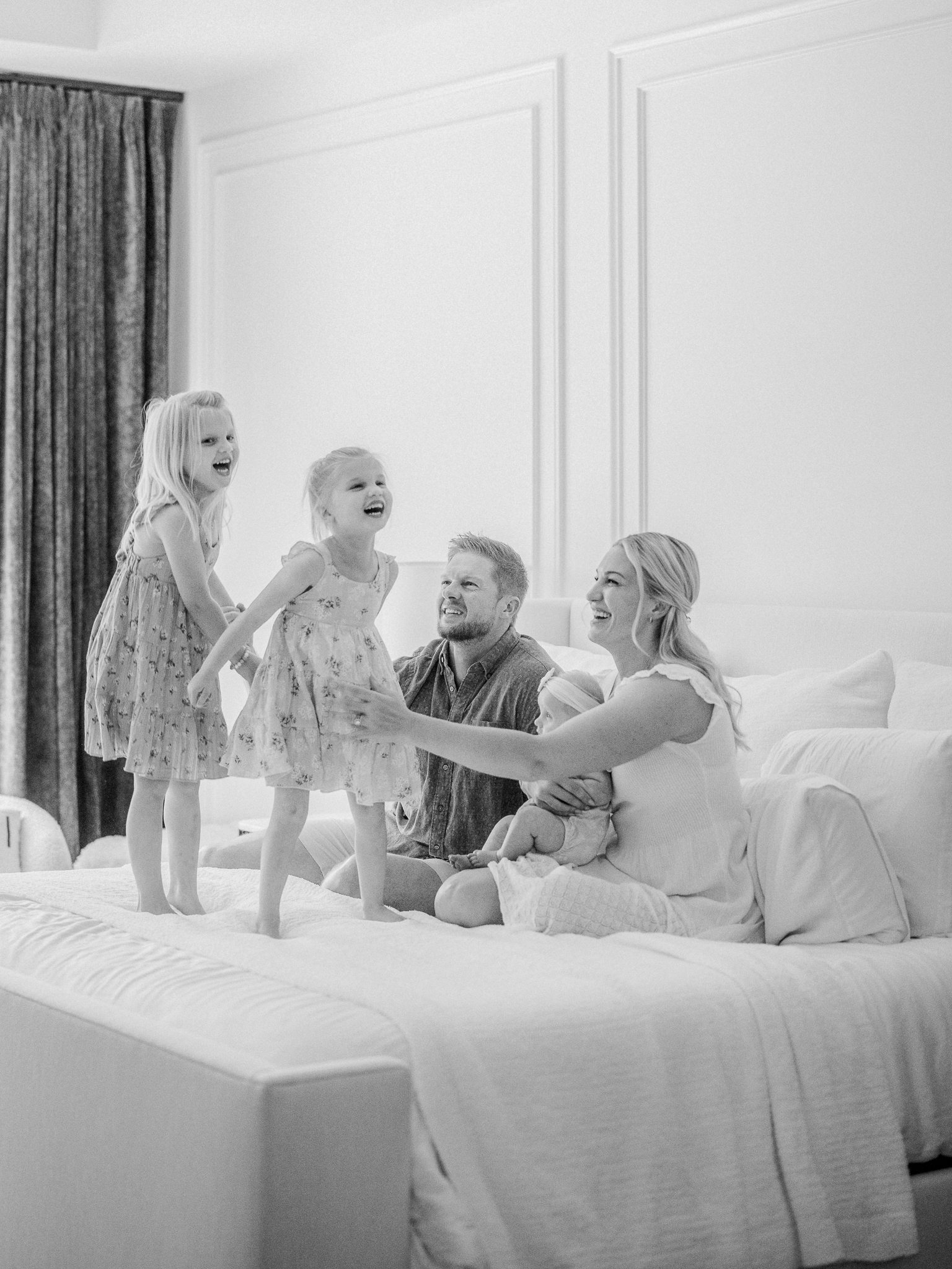 Big sisters laughing and playing on the bed during an in-home newborn photography session in Missouri with Love Tree Studios.