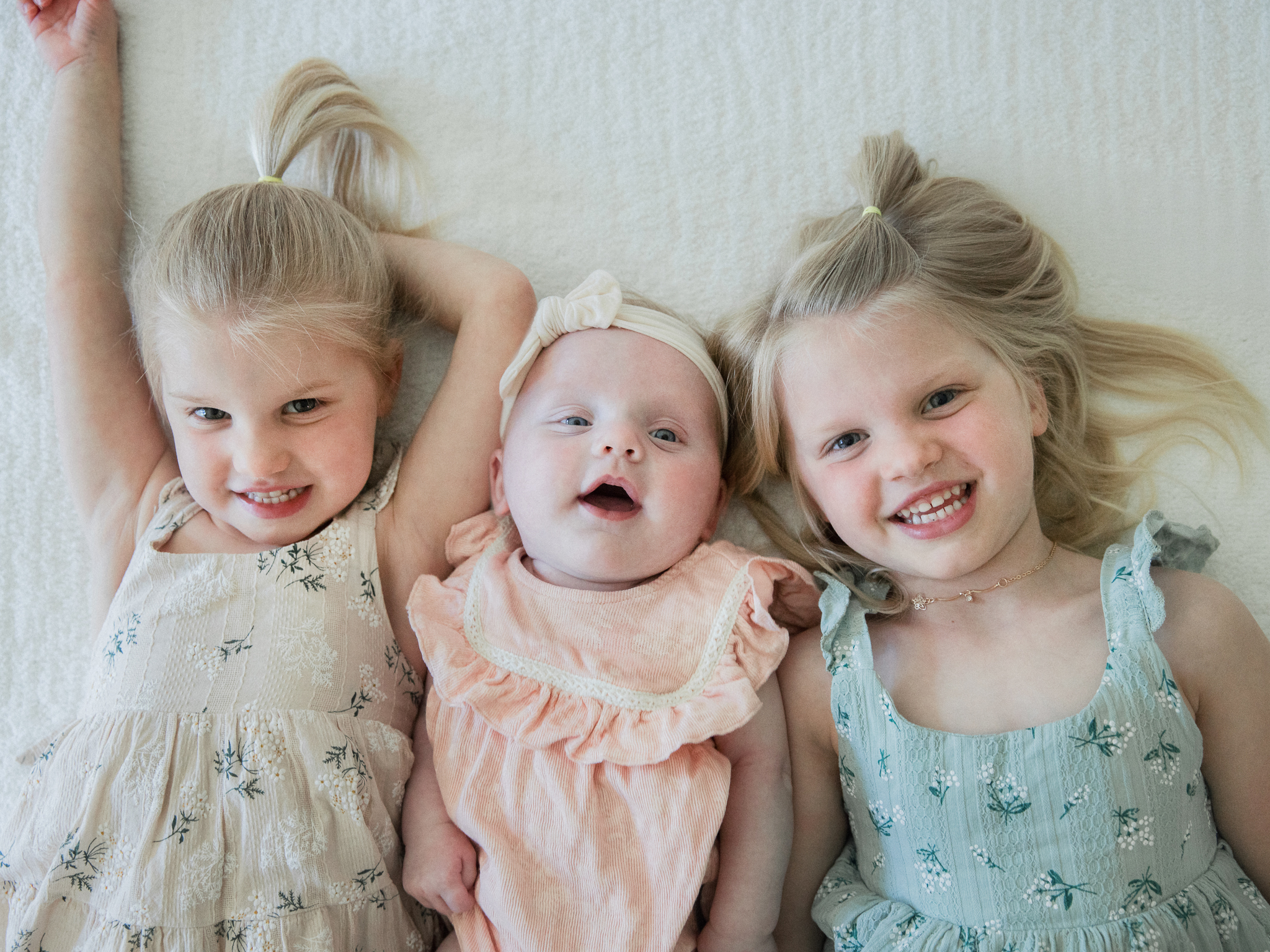Sisters laughing together while lying on the bed next to baby Lenny.