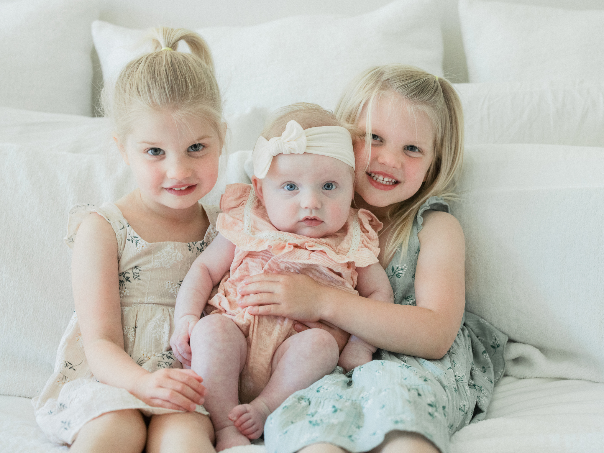 Big sisters lovingly holding newborn Lenny during an in-home newborn photography session in Missouri.