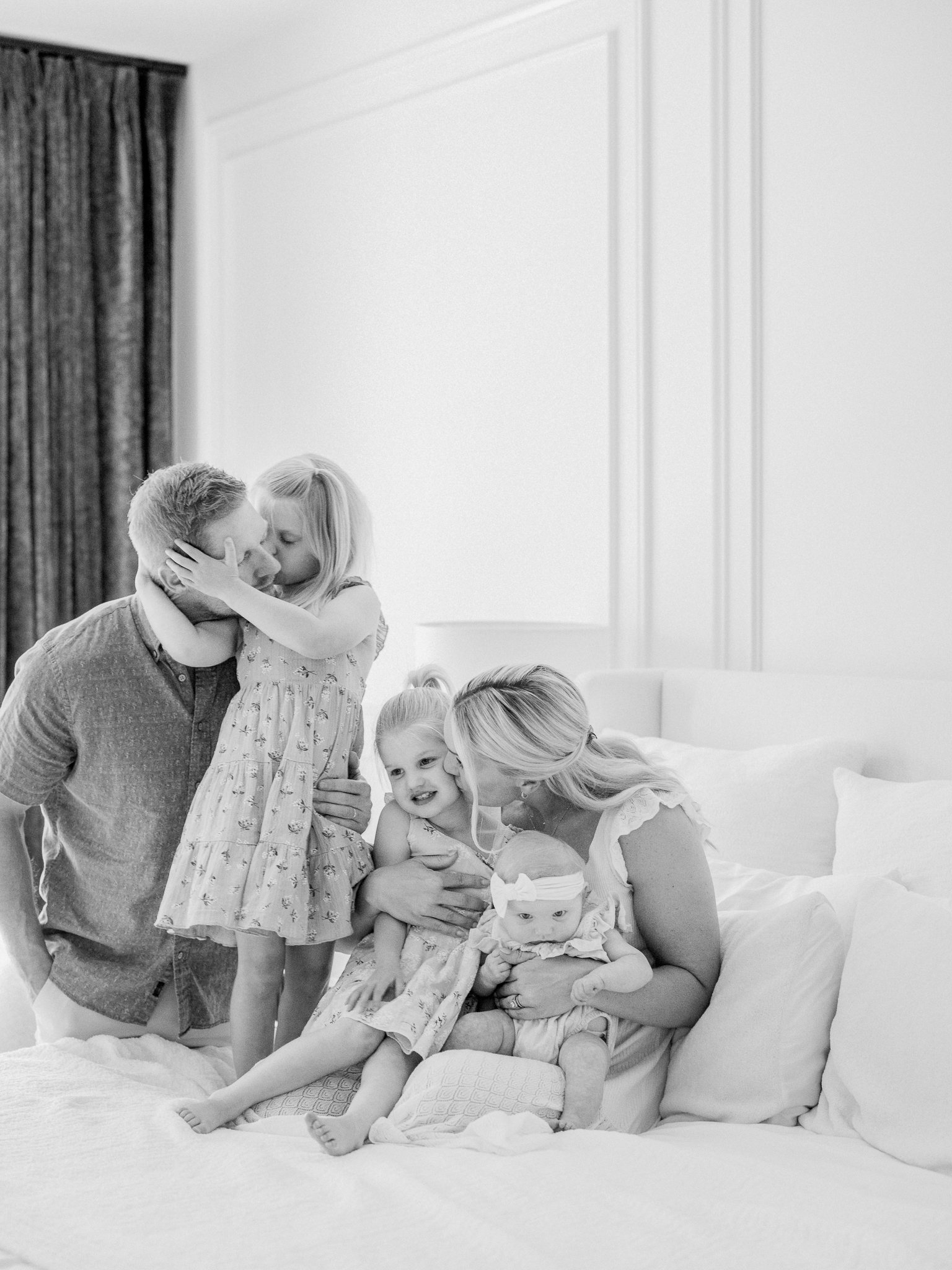 Heartfelt family moment during a Missouri in-home newborn session by Love Tree Studios, with daughters sharing kisses and cuddles.