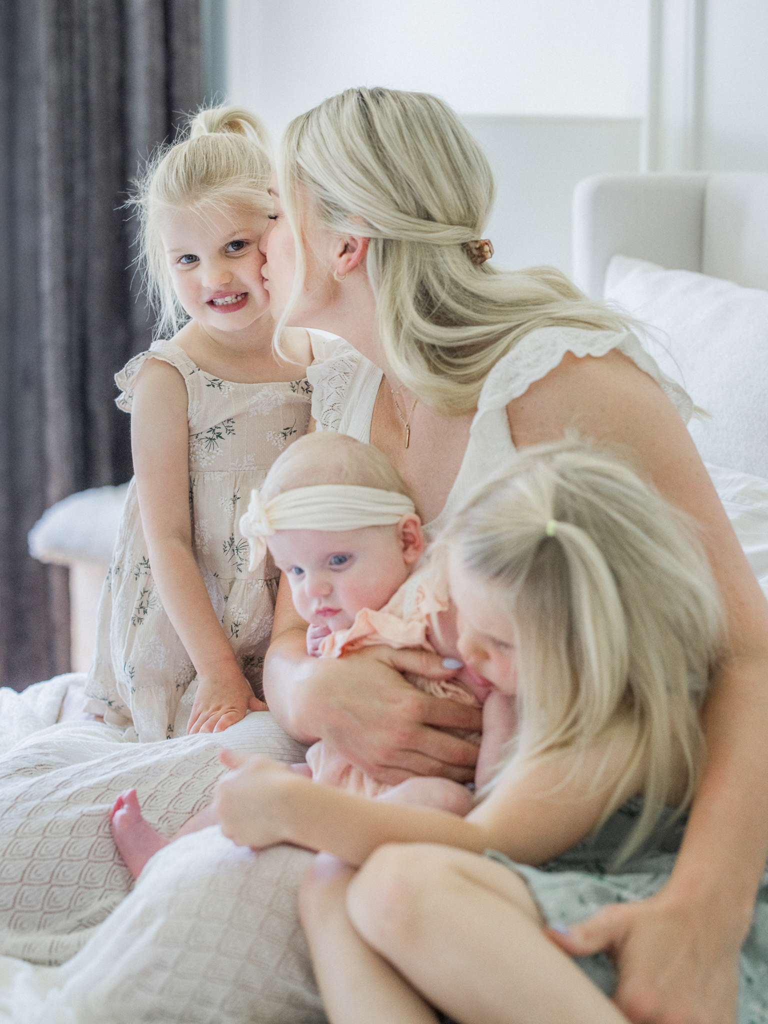 Sweet moment of a mother kissing her daughter’s cheek while holding baby Lenny, captured during a lifestyle newborn session in Missouri with Love Tree Studios.