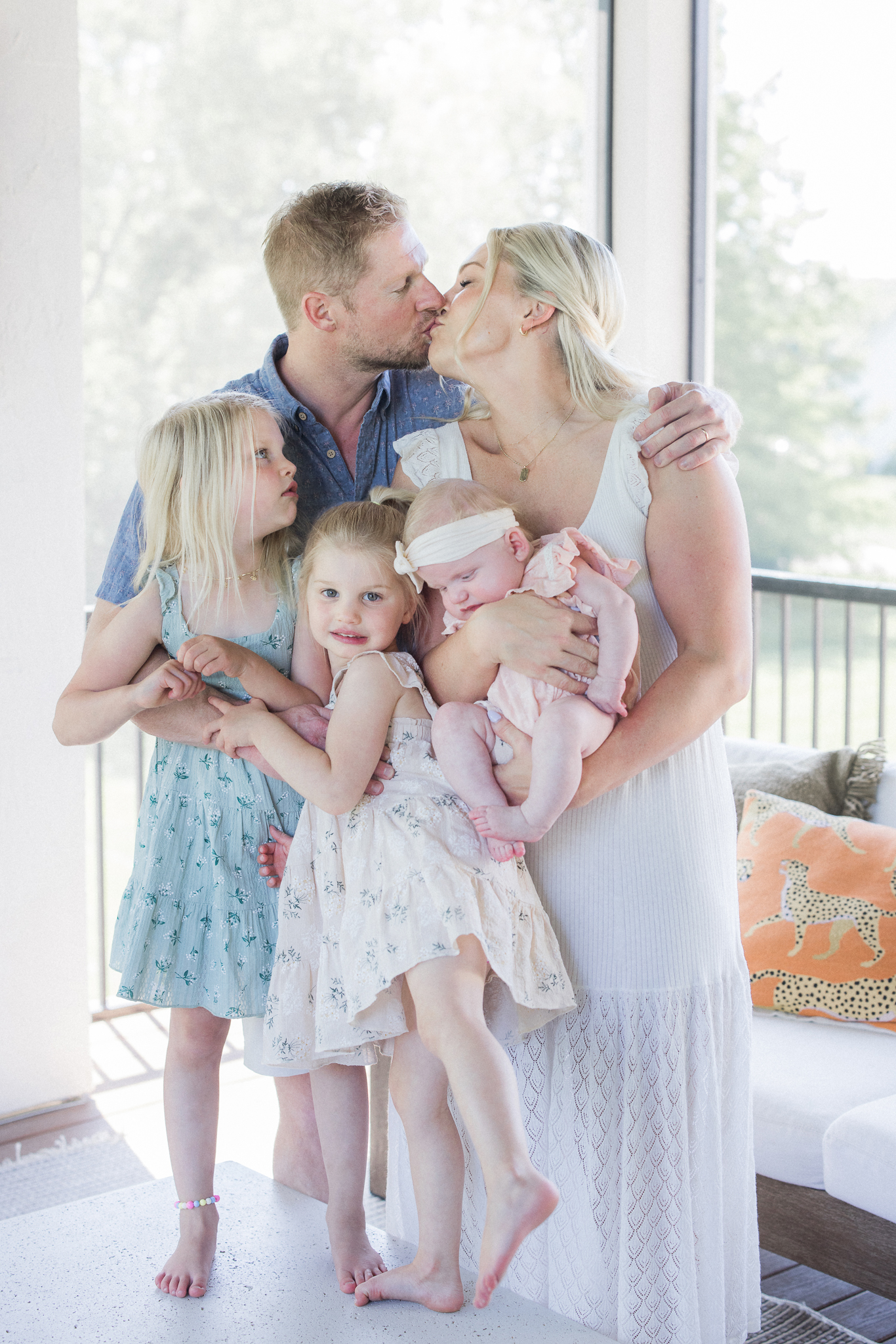 Parents kissing while holding baby and hugging daughters during a relaxed Missouri in-home newborn session by Love Tree Studios.