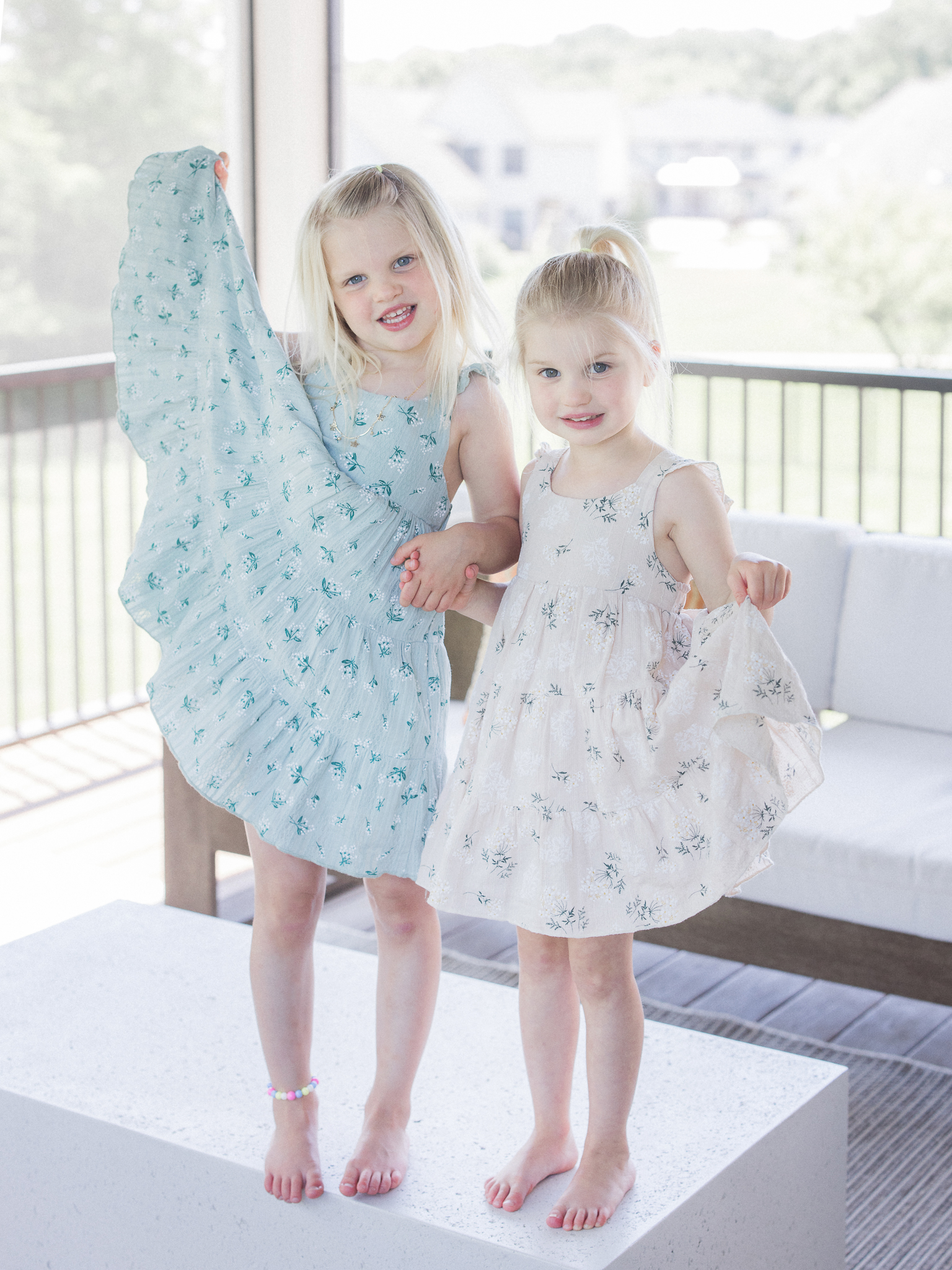 Sisters smiling and holding hands in matching dresses during a Missouri in-home newborn and family lifestyle session.