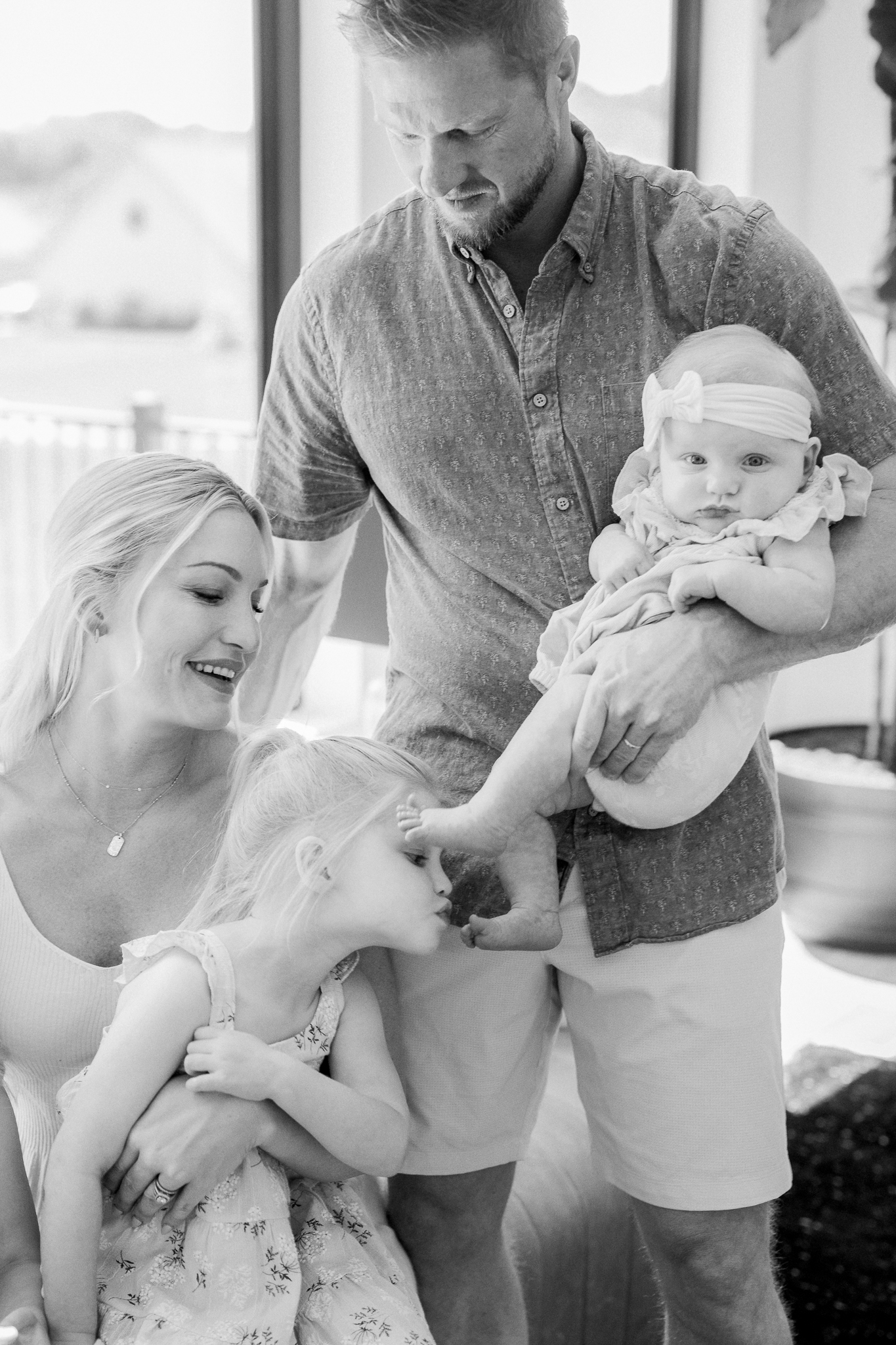 Sweet moment of big sister kissing baby’s foot during a natural lifestyle newborn photography session in Missouri with Love Tree Studios.