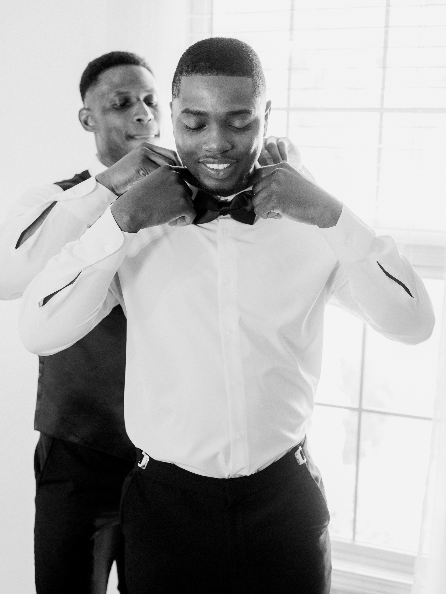 Groom getting help with his bow tie from his groomsman captured by Love Tree Studios for Jefferson City wedding photography in Jefferson City, Missouri.