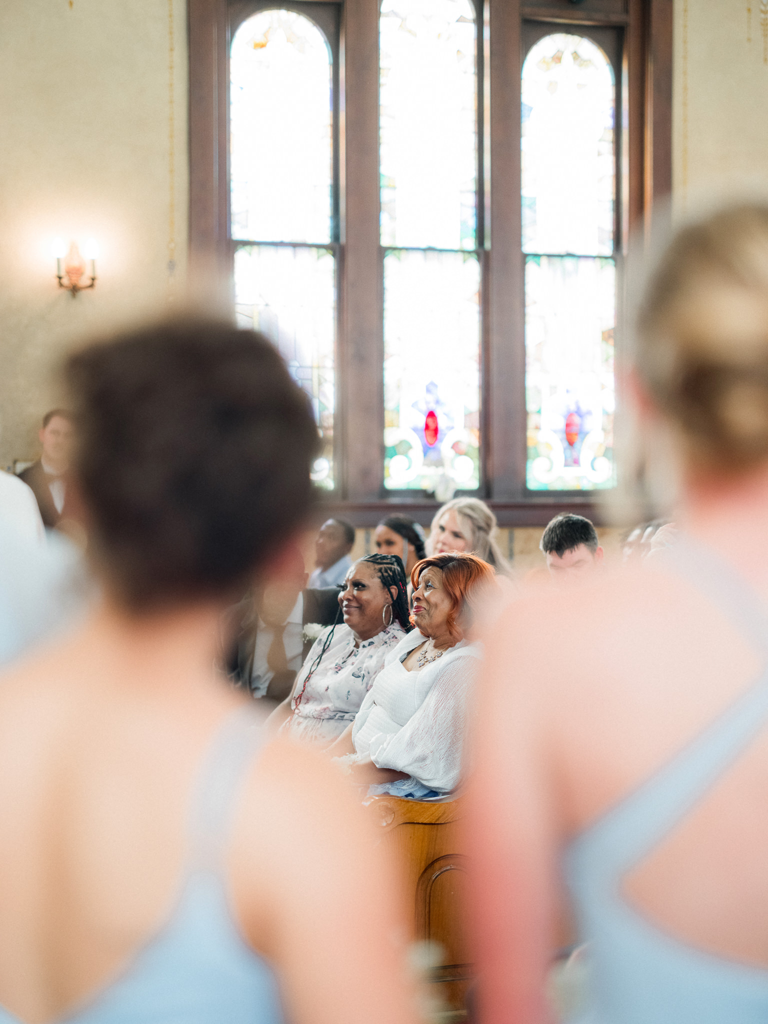 Guests seated in pews smile and watch the ceremony unfold, framed between bridesmaids — captured by Missouri wedding photographer.