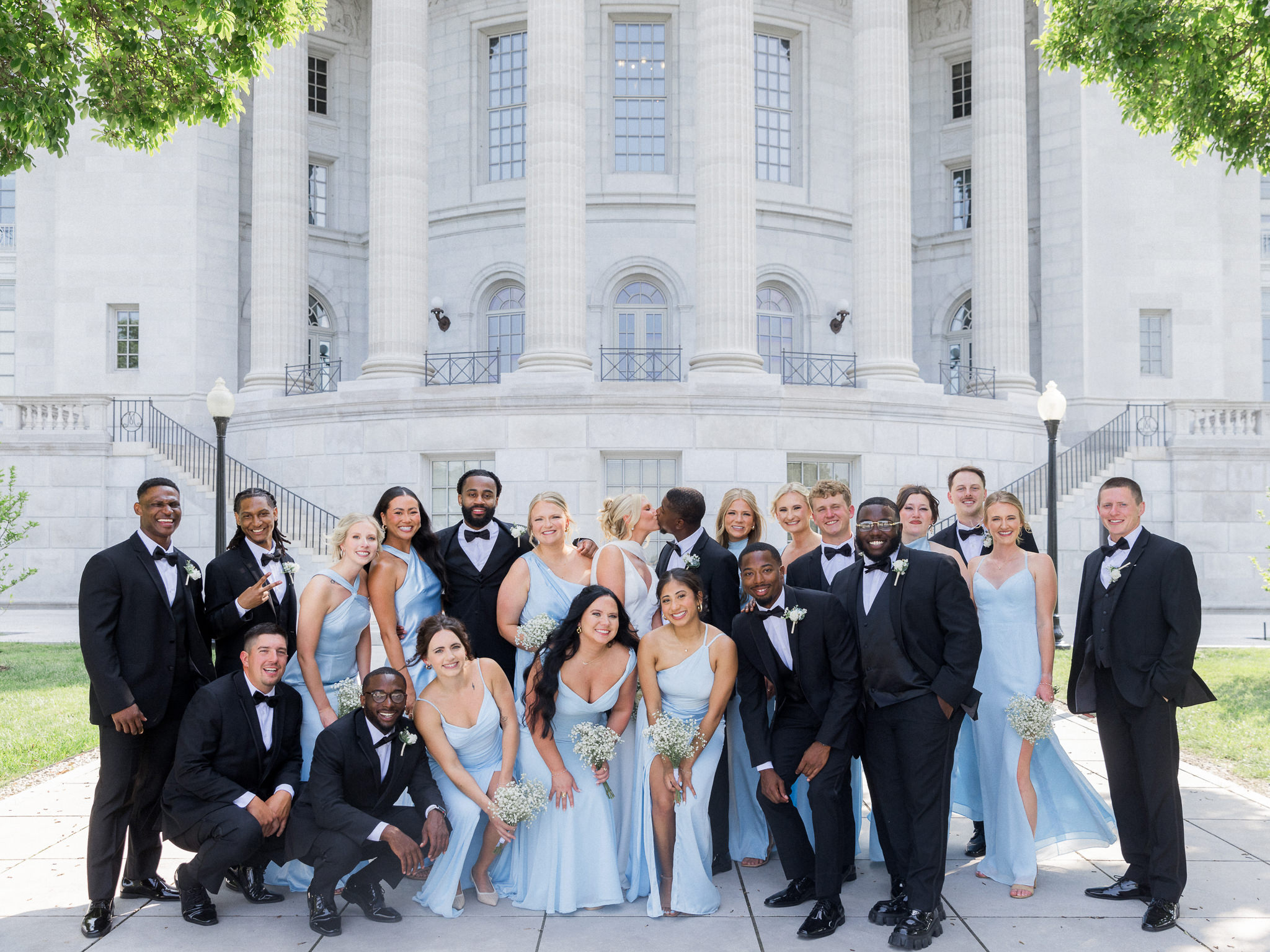 Large wedding party poses for a classic portrait outside a grand courthouse-style building.